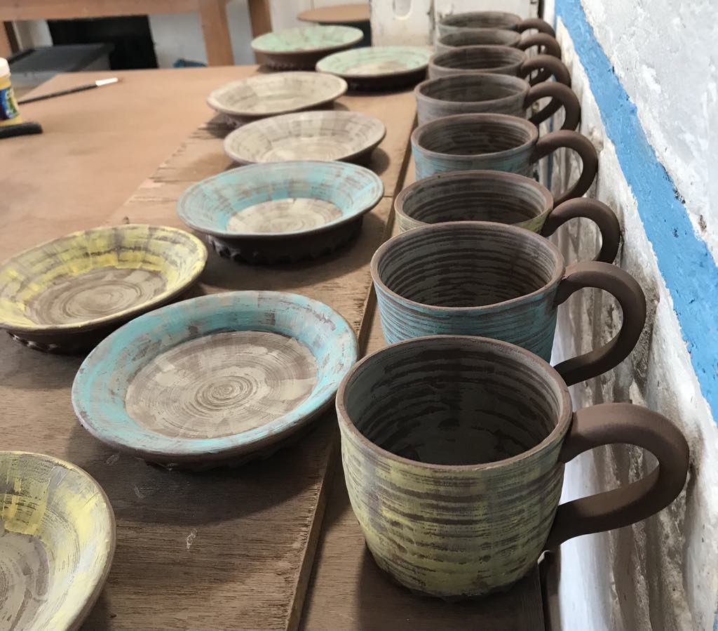 Clay cups and saucers on the making table at Eastnor Pottery made by Sarah Monk the pots have had a layer of slip brushed on.