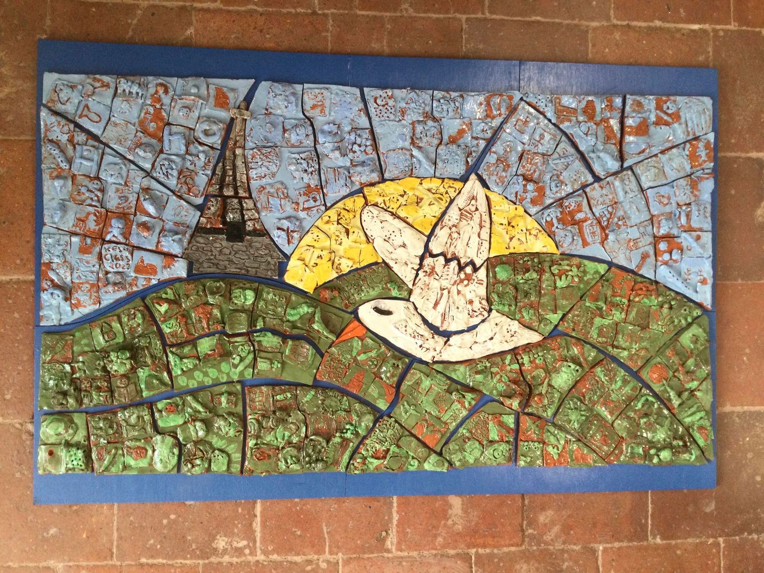 cleobury mortimer primary school logo made from pottery tiles created by the school children. It depicts a white bird flying over the hills and church tower with the sun setting