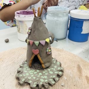 clay hand modeled tepee surrounded with multicoloured bunting and red heart on top of door with a green base