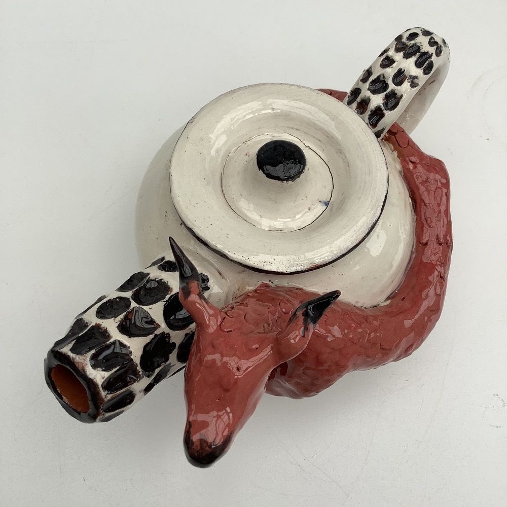 white hand thrown tea pot with black spotted spout, surrounded by hand modeled red dragon taken from a birds eye view