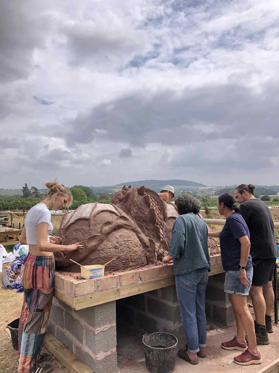 five adult volunteers at growing local hereford creating a cob dragon pizza oven