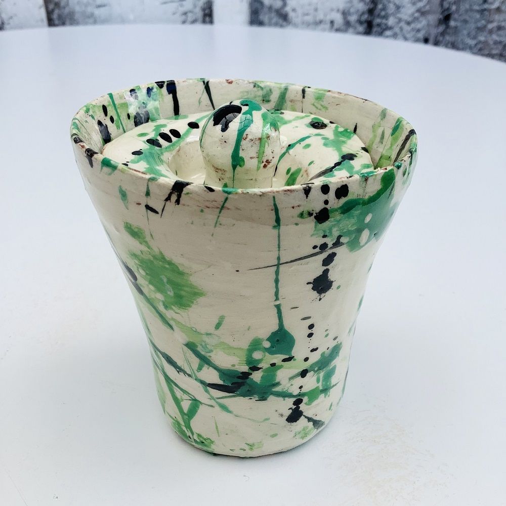 small lidded pot in the shape of a conical beaker glazed white with green and black splatted pattern made by potter's wheel course participant at eastnor pottery in herefordshire