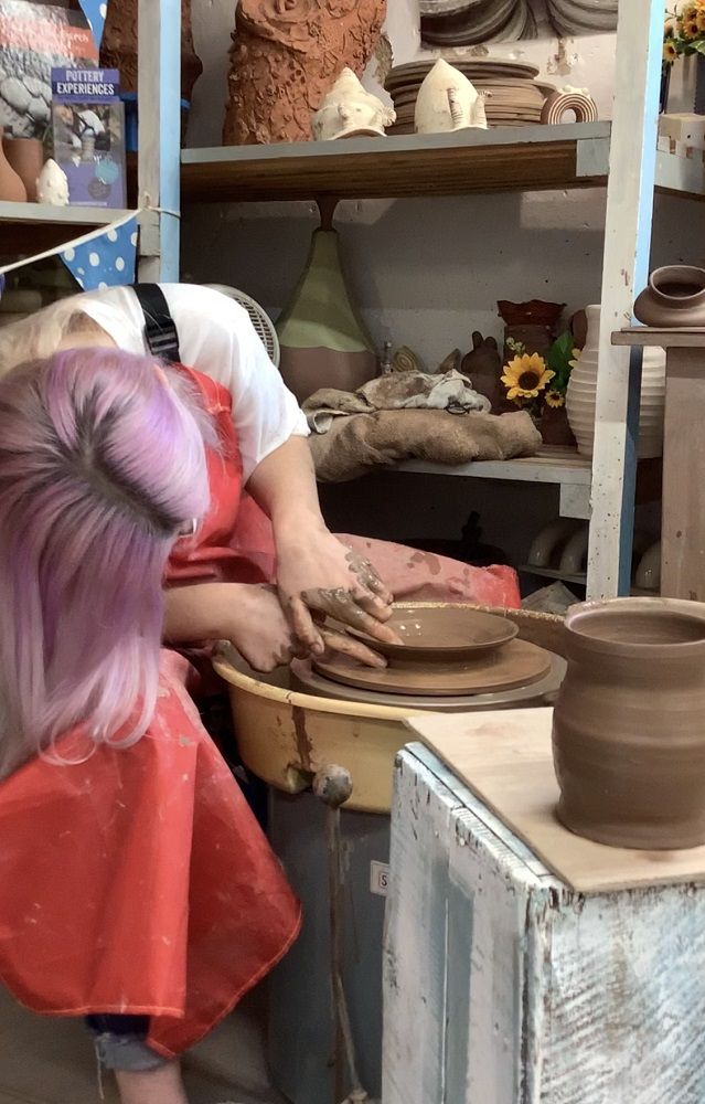 lady throwing plate on weekend pottery course leaning over to throw