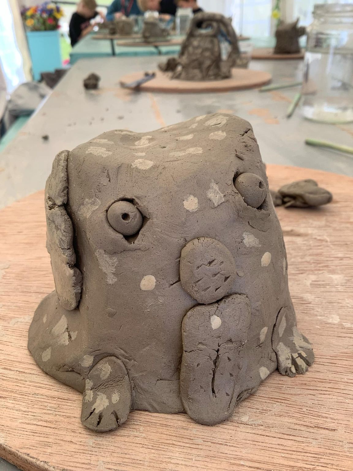 a clay dog made by a child with spots of white slip painted onto the surface