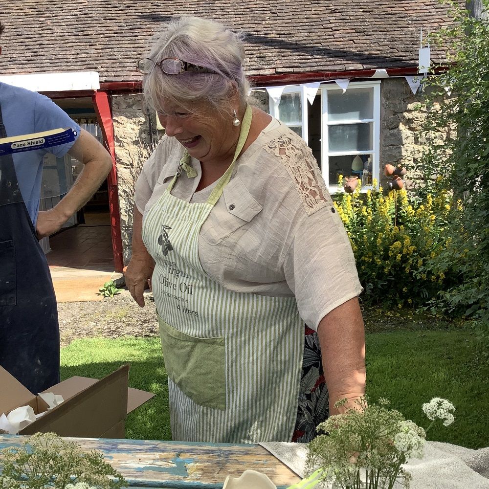 lady holding on to wooden table laughing with pottery in the background