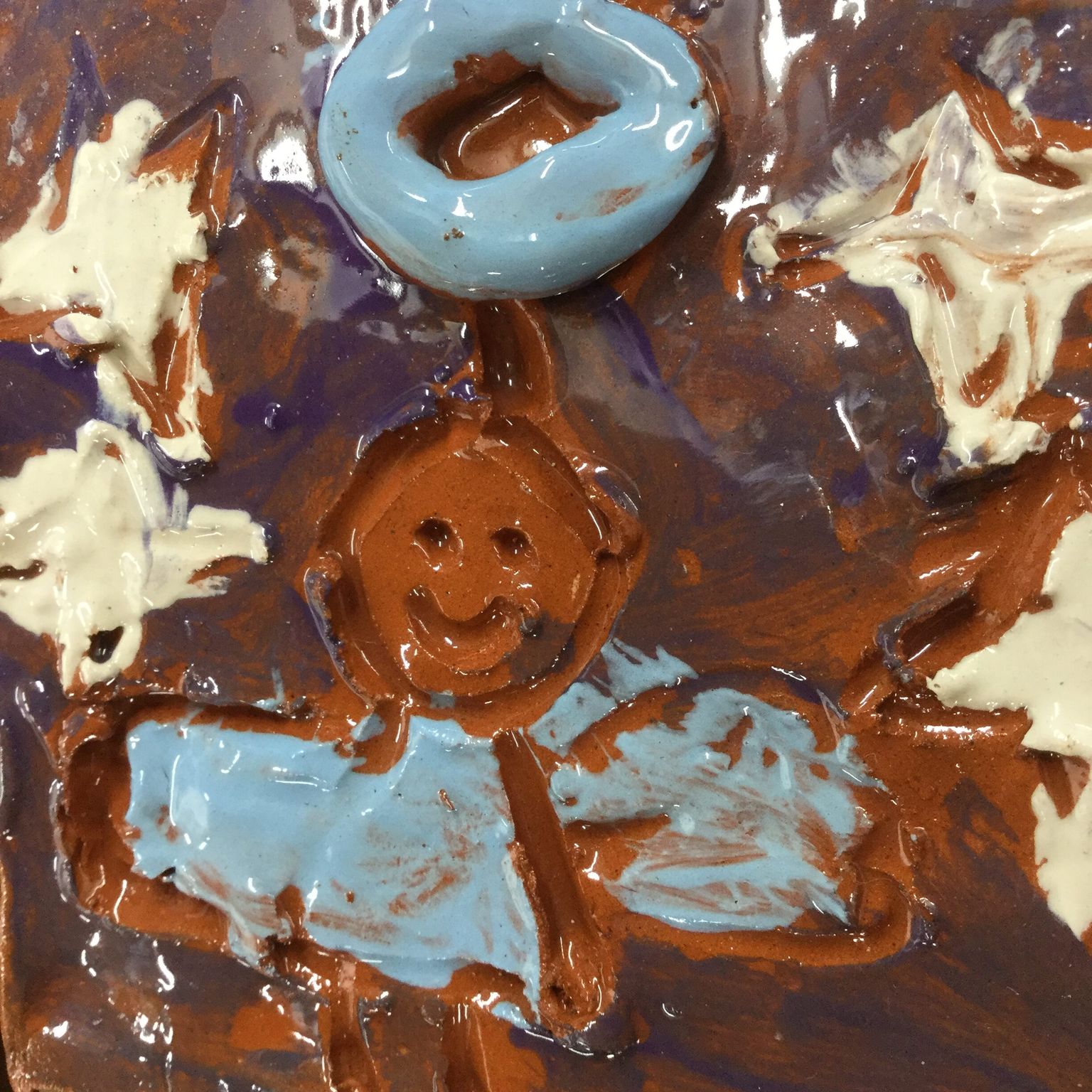 clay tile depicting an angel made by a primary school child. The angel and halo are light blue and its flying through a purple sky with white stars