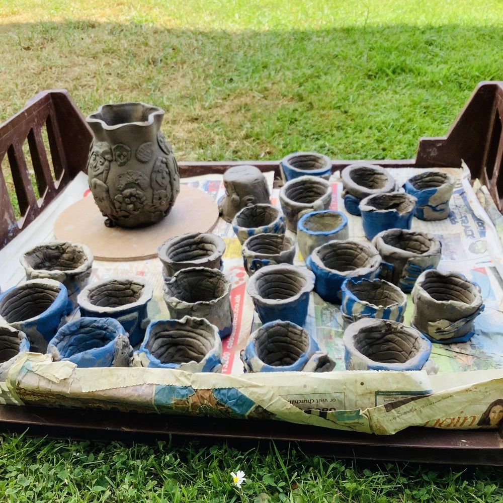 plastic tray holding coil clay pots painted blue and a larger pot decorated with 3D faces