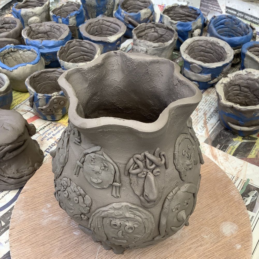 clay pot dcorated with 3D faces and coil clay pots in the background