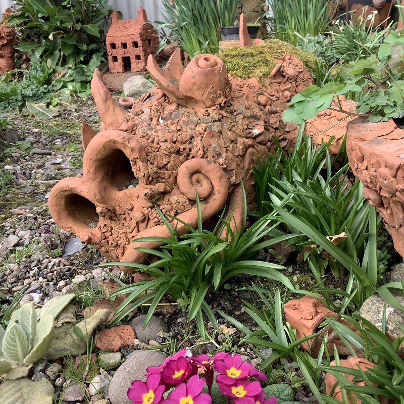 collaborative terracotta dragon lounging in the flower border at eastnor pottery and the flying potter herefordshire