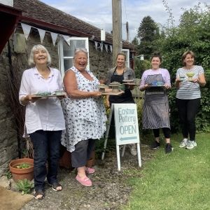 five women holding wodden boards with ceramic creations they have made standing outside eastnor pottery next to the eastnor pottery sign