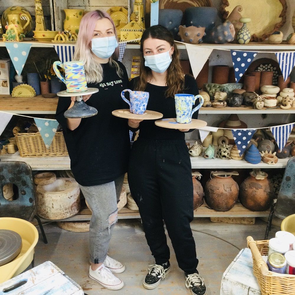 two best friends taking part on weekend pottery course holding pots they made