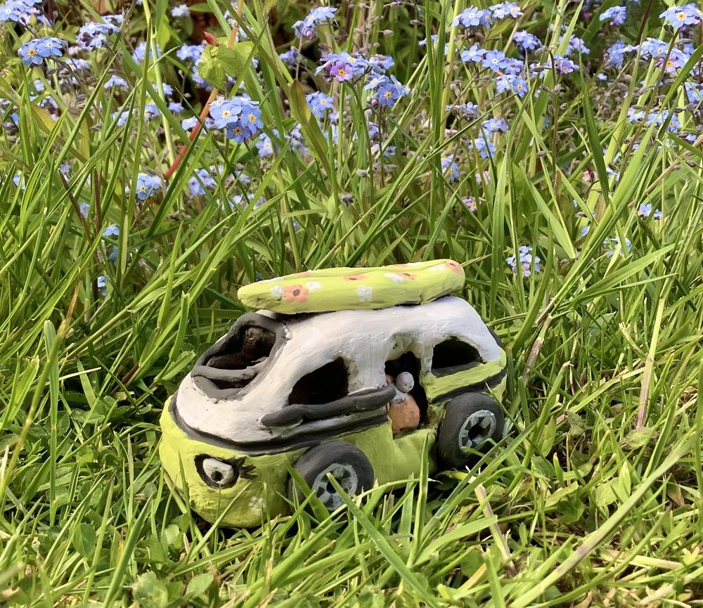 clay handmade campervan painted green on grass with flowers in the background