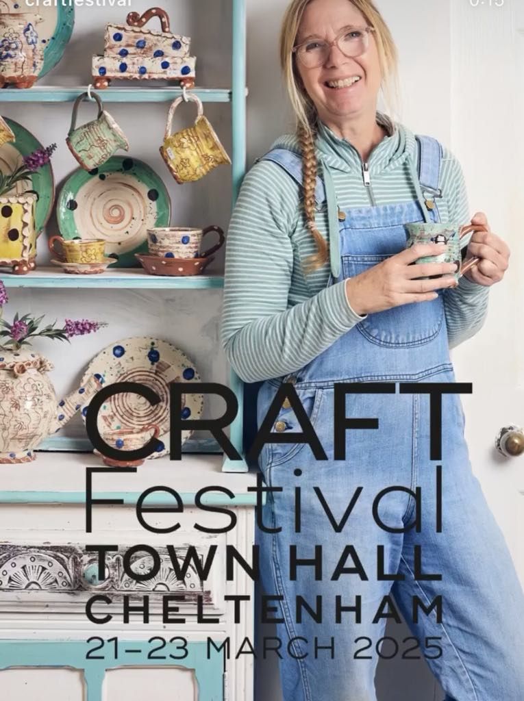 Sarah Monk in her studio at Eastnor Pottery. She is stood, leaning against a cabinet dresser containing her pottery. She is holding a mug and smiling at the camera.