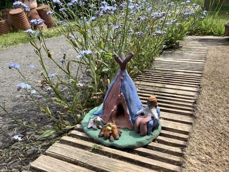 clay hand modeled tepee red and blue with person sat on a chair, fire and a white dog