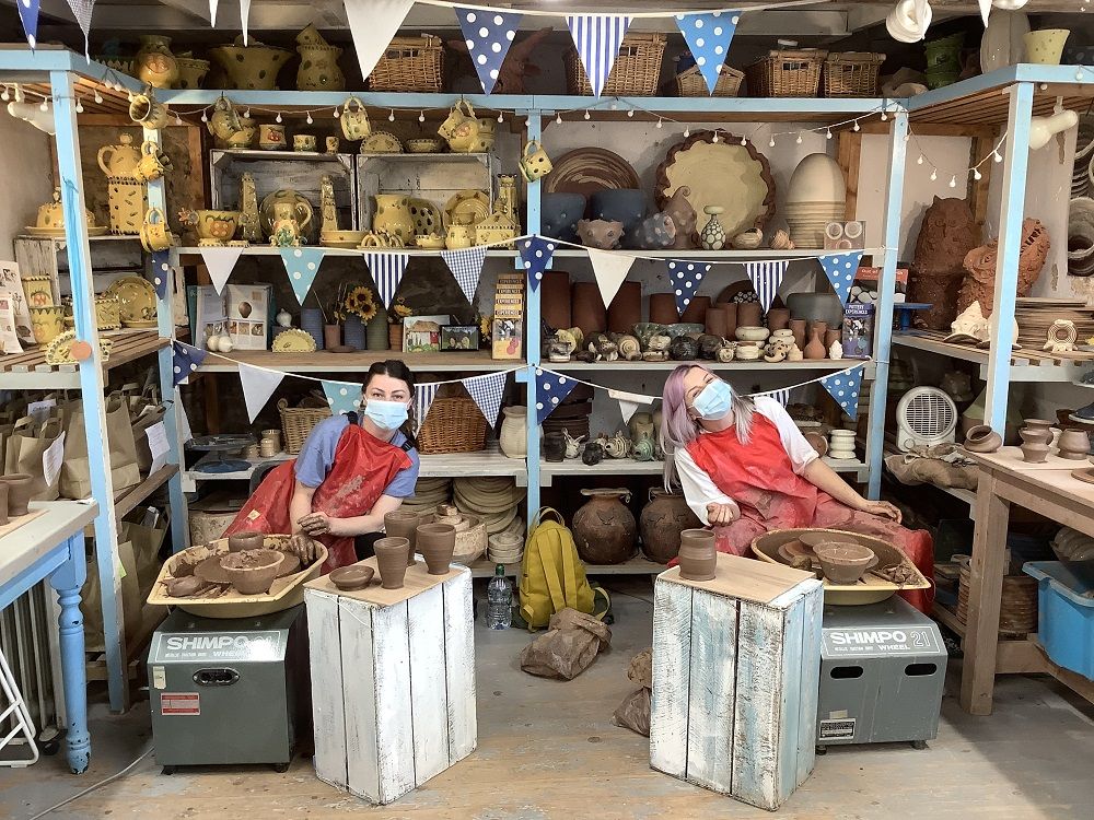 two friends taking part in pottery weekend course on their wheels throwing pots