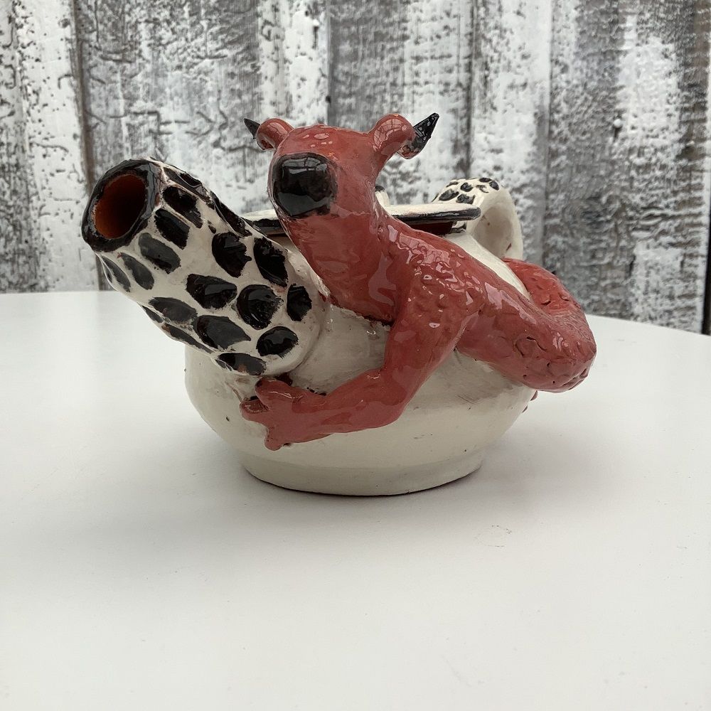 white hand thrown tea pot with black spotted spout, surrounded by hand modeled red dragon