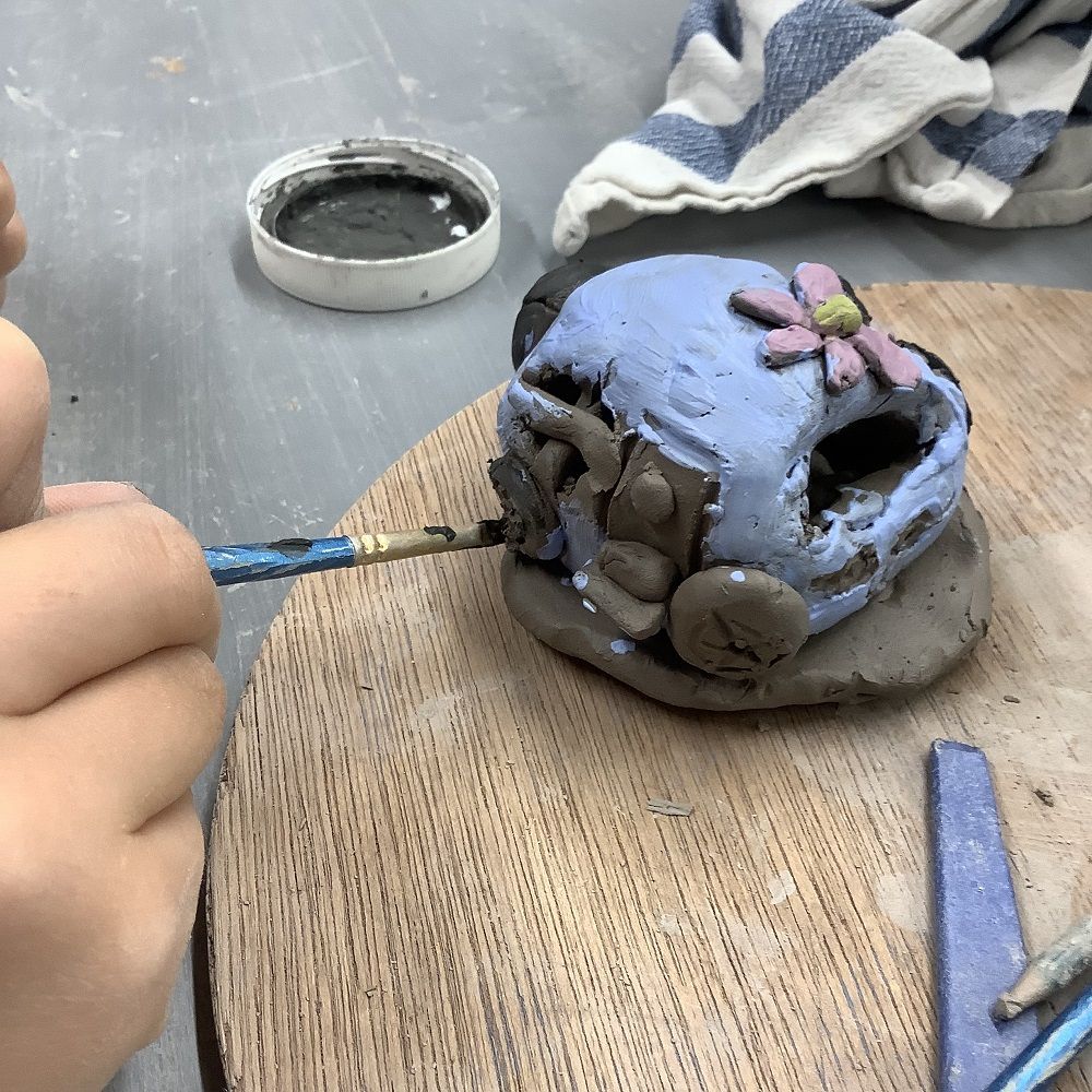 child's hand holding painting brush, painting a purple hand modelled camper van made from clay