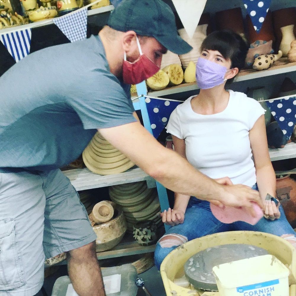 couple taking part in an introduction to the potter's wheel helping one another clean the wheel 