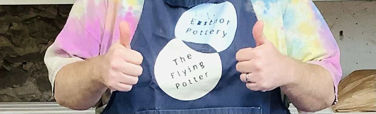 pair of hands in the thumbs up position raised in front of a torso wearing a blue apron with an eastnor pottery logo