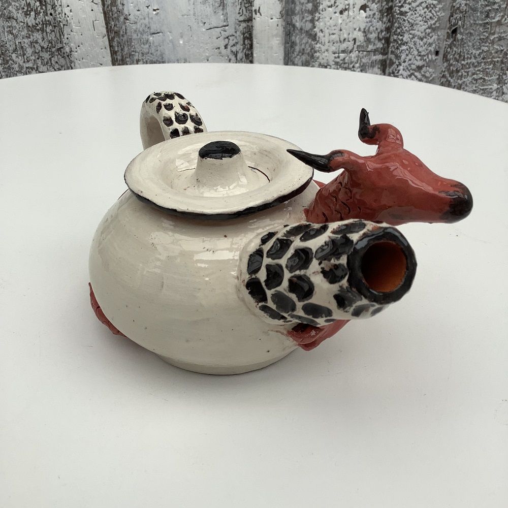 white hand thrown tea pot with black spotted spout, surrounded by hand modeled red dragon