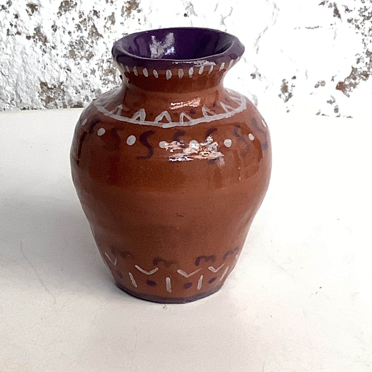 traditional vase shaped glazed terracotta vase with purple inside and a combination of dots, S shaped squiggles and bunting lines painted in white and purple on the outside. The little 10 cms pot was made on a potter's wheel weekend course at eastnor pottery in Herefordshire