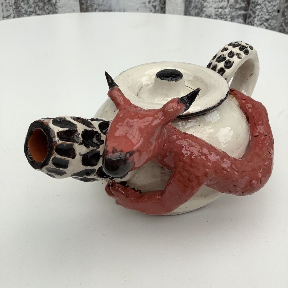 white hand thrown tea pot with black spotted spout, surrounded by hand modeled red dragon