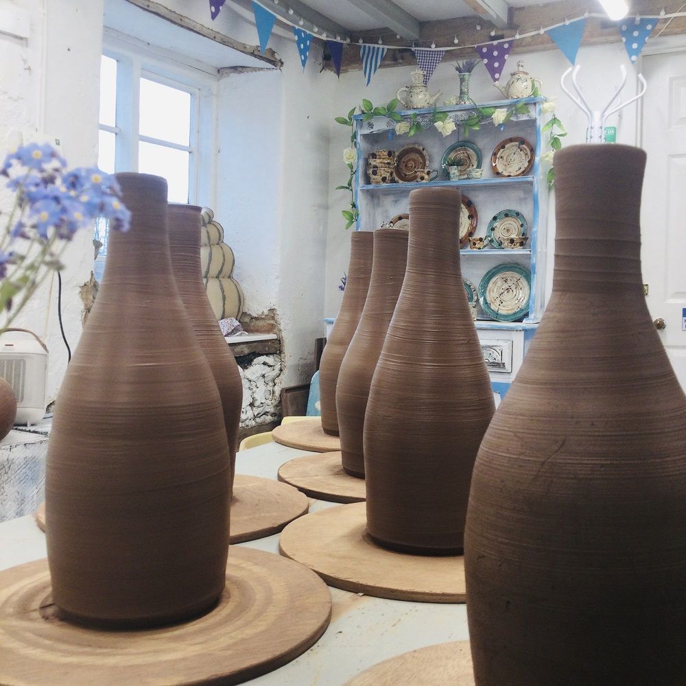 thrown terracotta bottles lined up and drying in pottery studio