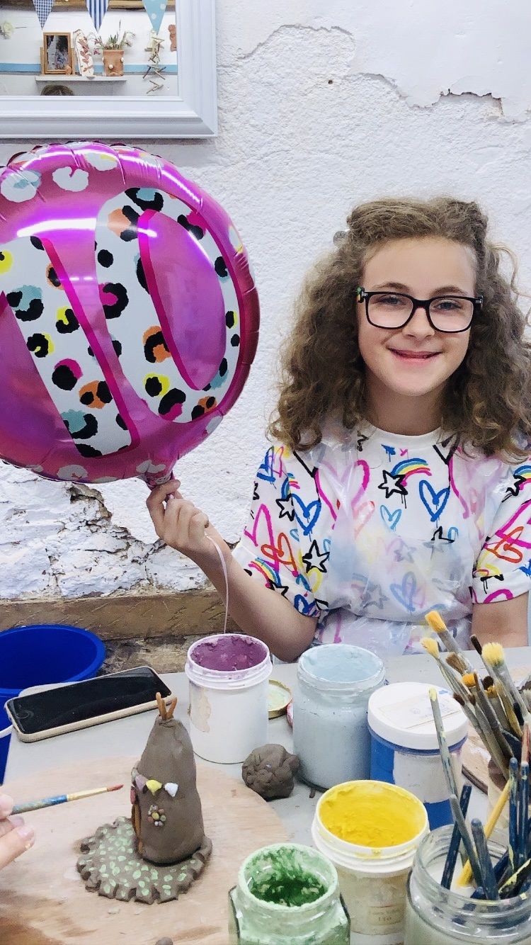 child holding pink 10th birthday baloon next to clay creation made at eastnor pottery