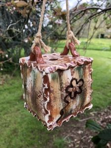 dangly pottery flower brick made by potter sarah monk hanging from a tree on a short piece of natural rope at sculpture at kingham lodge exhibition.