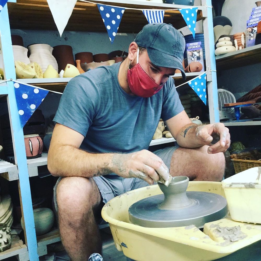 man taking part in a potter's wheel introduction using sponge to clean up pot thrown on the potter's wheel