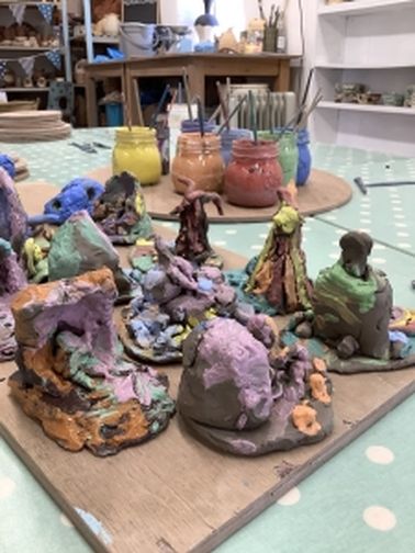 selection of modeled clay painted with glazes, create by children with glazes in the background