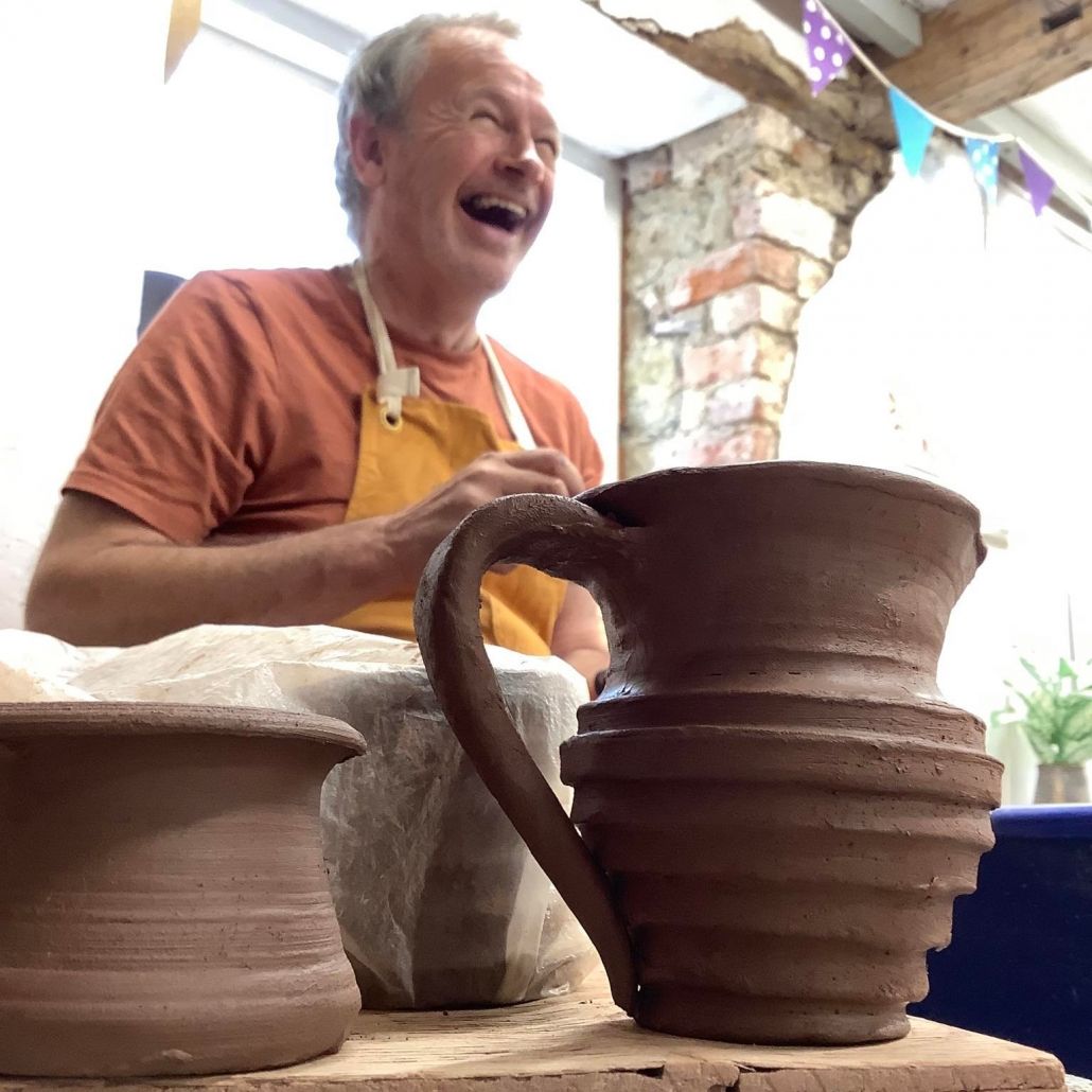 A man laughing and enjoying his pottery course at eastnor pottery with a freshly thrown clay jug in front of him