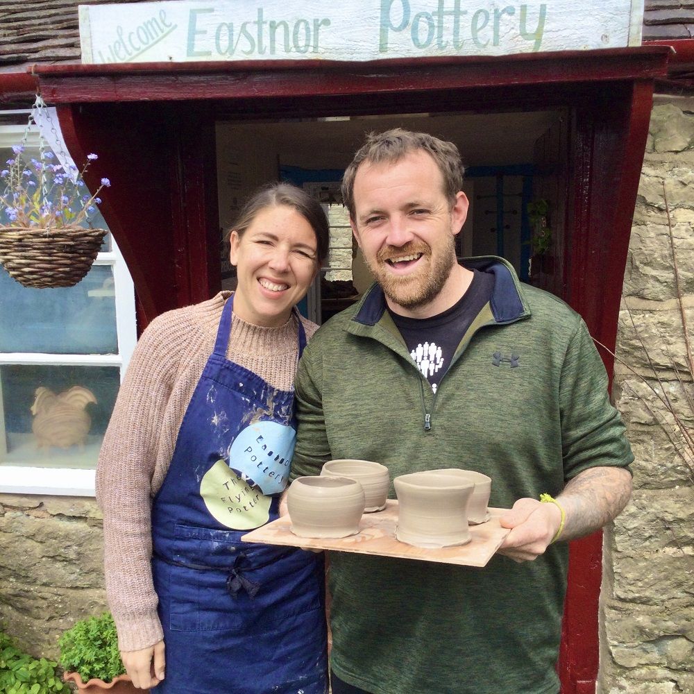 couple standing in doorway of pottery holding pots made at eastnor