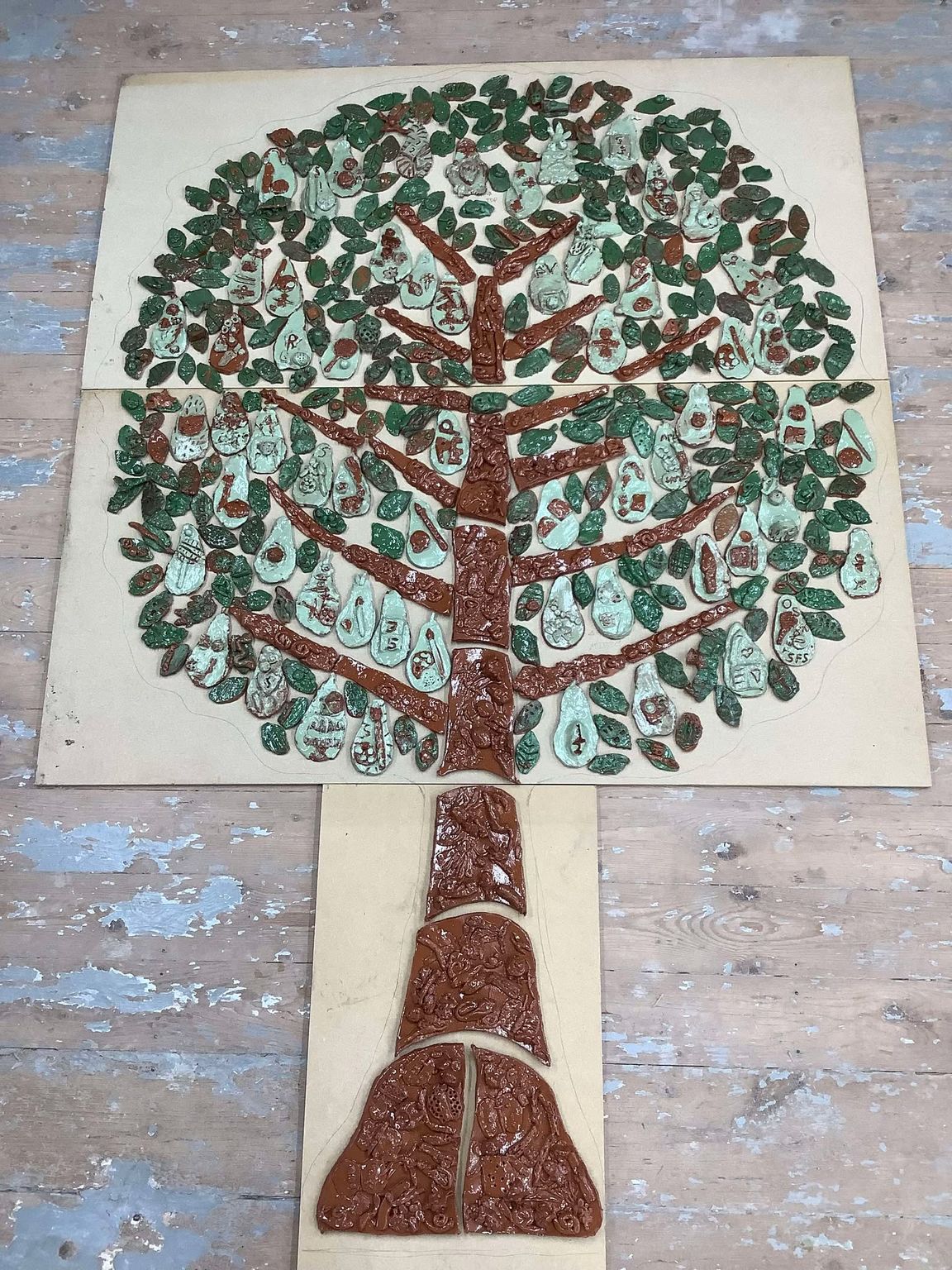 lots of green pottery leaves made by primary school aged children arranged in the shape of a giant tree tile panel