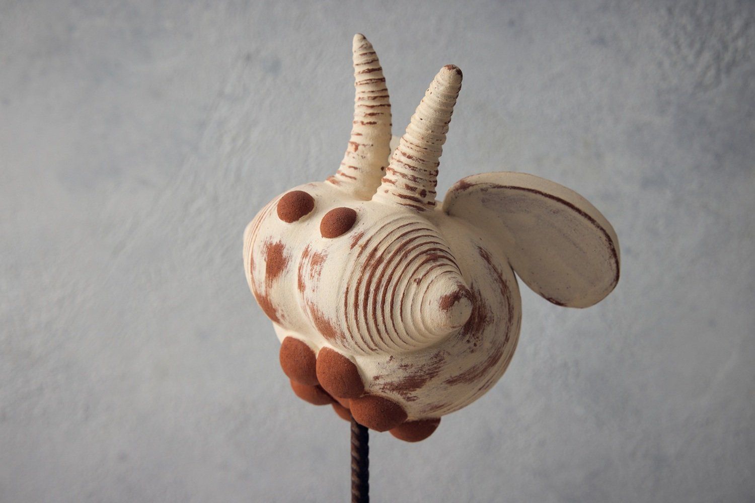 A pottery bug on a metal stick. Made from terracotta and brushed roughly in white. This highly stylised bug has curly antennae, wings and round terracotta eyes. It also has 6 round terracotta feet.