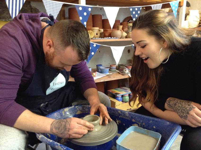 couple watch each other make a pot on the potter's wheel at eastnor pottery herefordshire