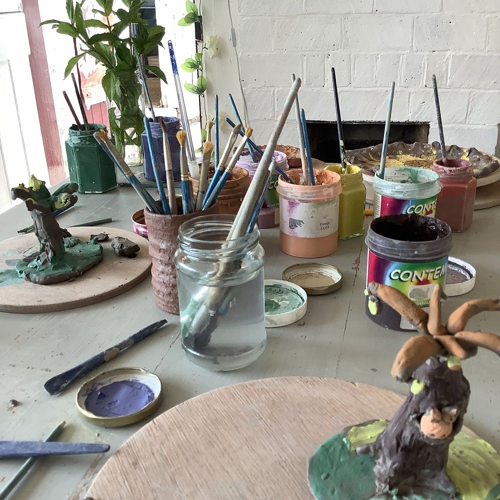 table with pots of glazes and water with paintbrushes inside after a clay modelling session