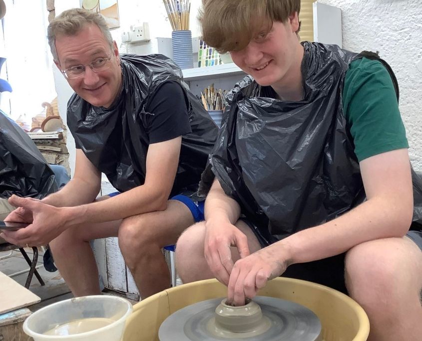 father and son sat on the potter's wheels at eastnor pottery dressed in black bin bags to protect their clothes from clay splats