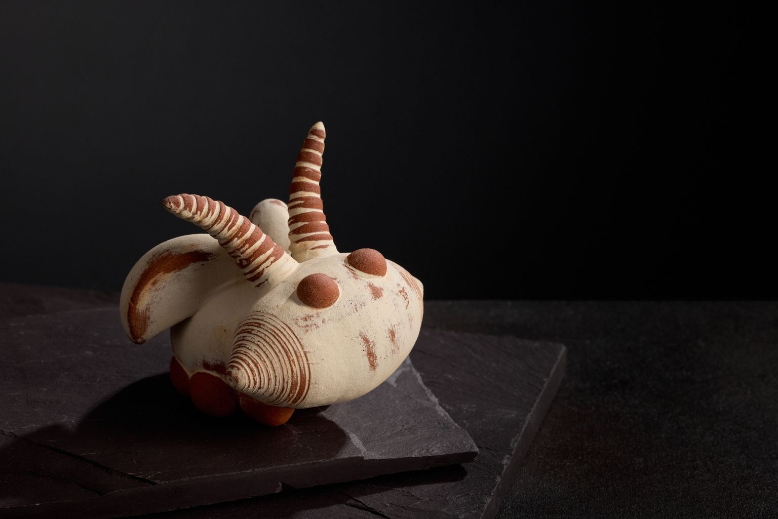 small bug eyed bug rattle made by artist potter jon williams. it is mostly cream with terracotta antanae and terracotta bulging eyes. photographed on a black slate background