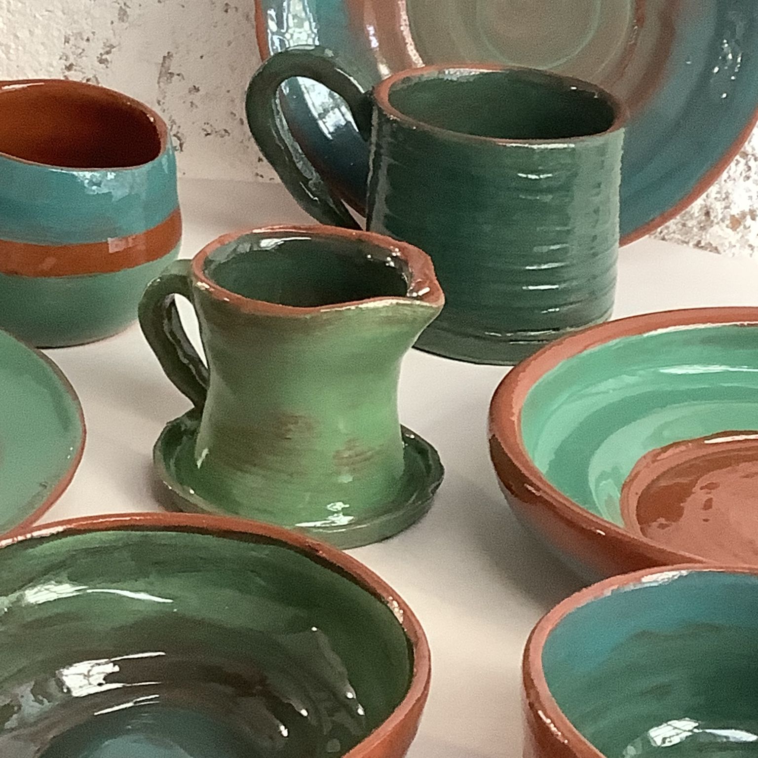 green and terracotta hand made mugs and plates created on the potter's wheel by pottery course participant