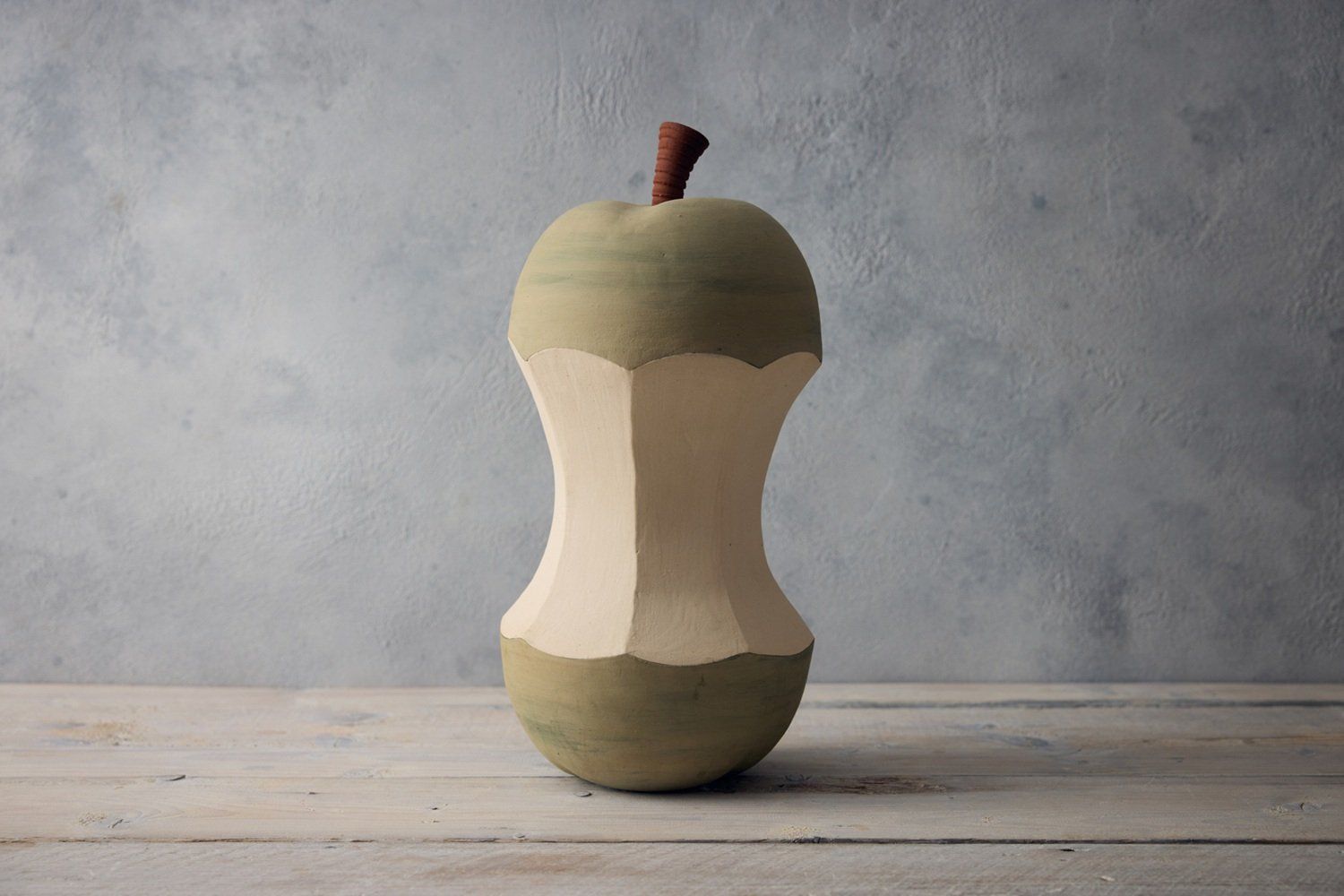 A sculptural ceramic pear core made by Jon Williams. The pear is light green, the core is faceted in a cream colour and the rear stem is terracotta.