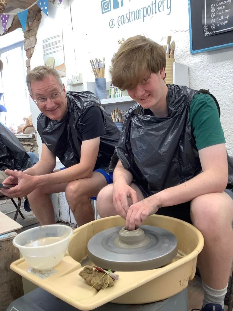 father and son sat on the potter's wheels at eastnor pottery dressed in black bin bags to protect their clothes from clay splats