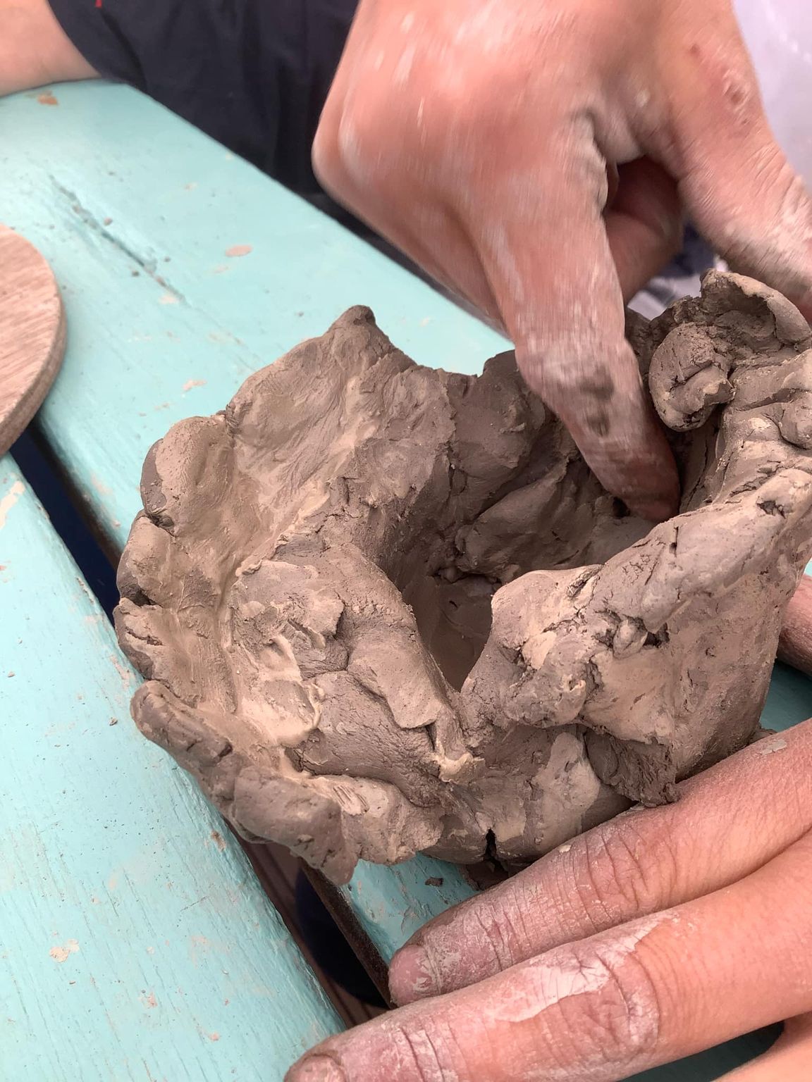 child's hands manipulating a coil pot at eastnor pottery. The fingers are covered in dry clay and they are pinching the material between finger and thumb