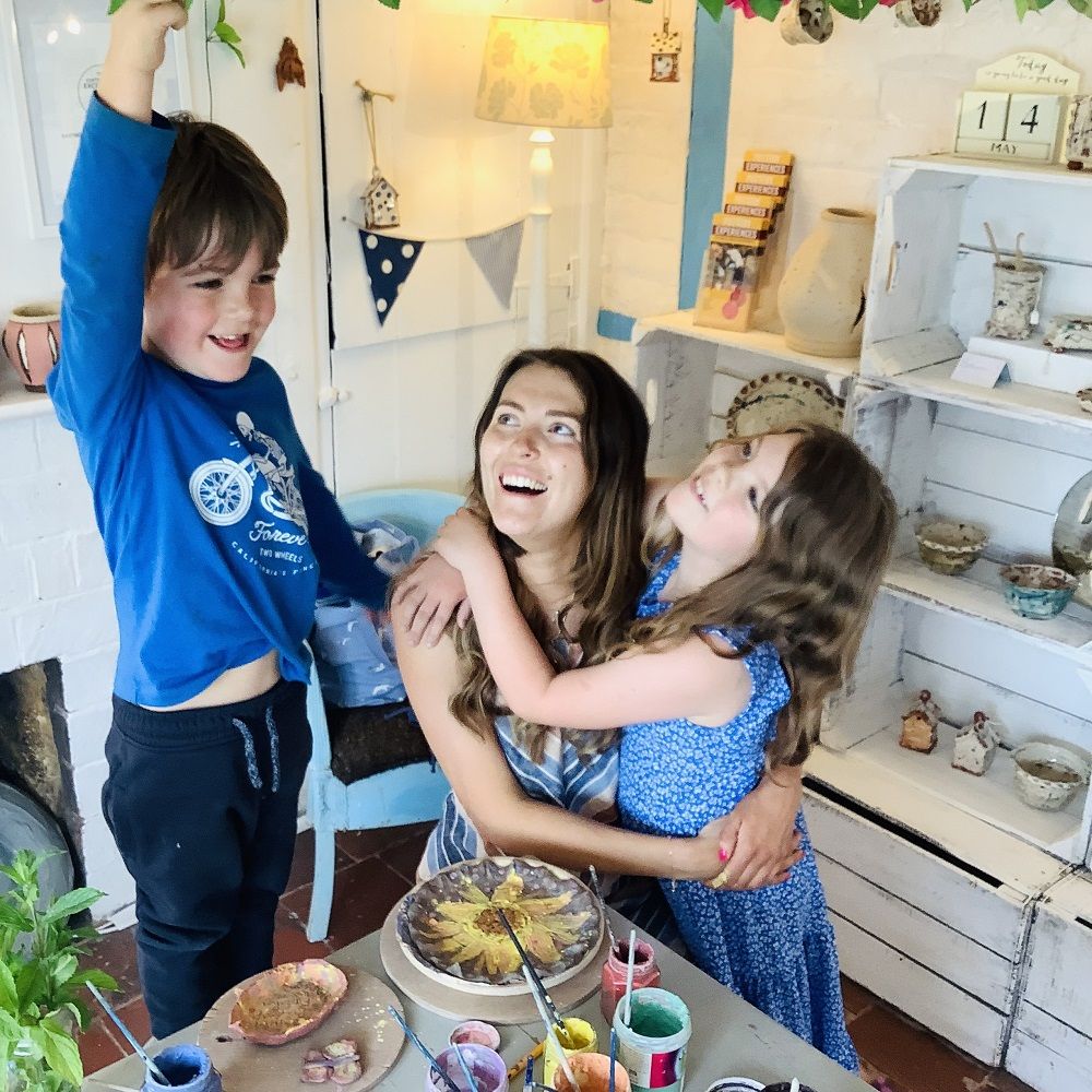 mother with son and daughter embracing next to clay creations made at eastnor pottery