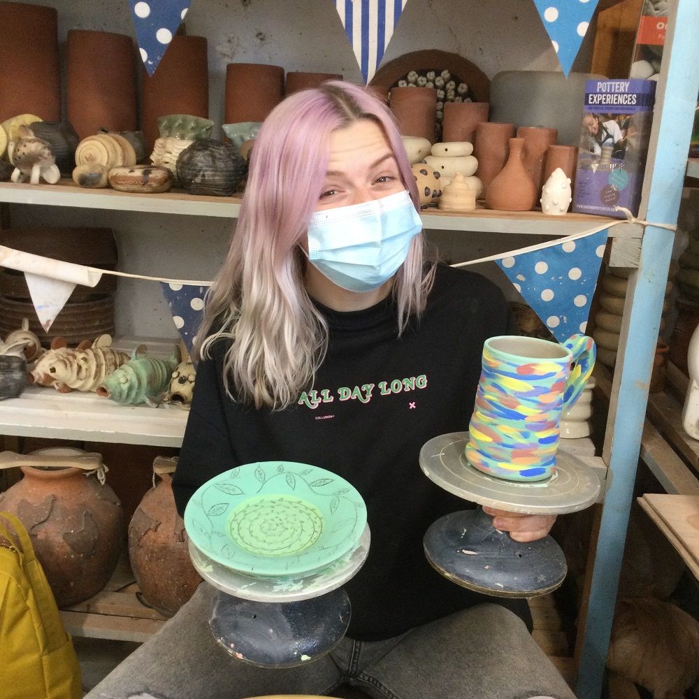 lady holding a painted mug and plate made on weekend pottery course